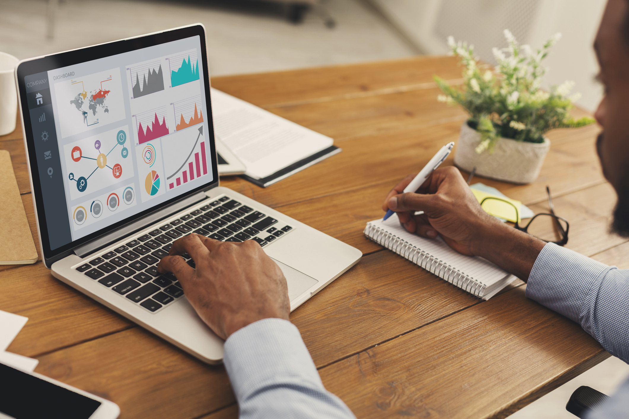 Close up back view of black business person analyzing graph on laptop and writing in notepad