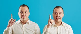 Young adult Caucasian twins wearing white shirts having idea, blue wall background