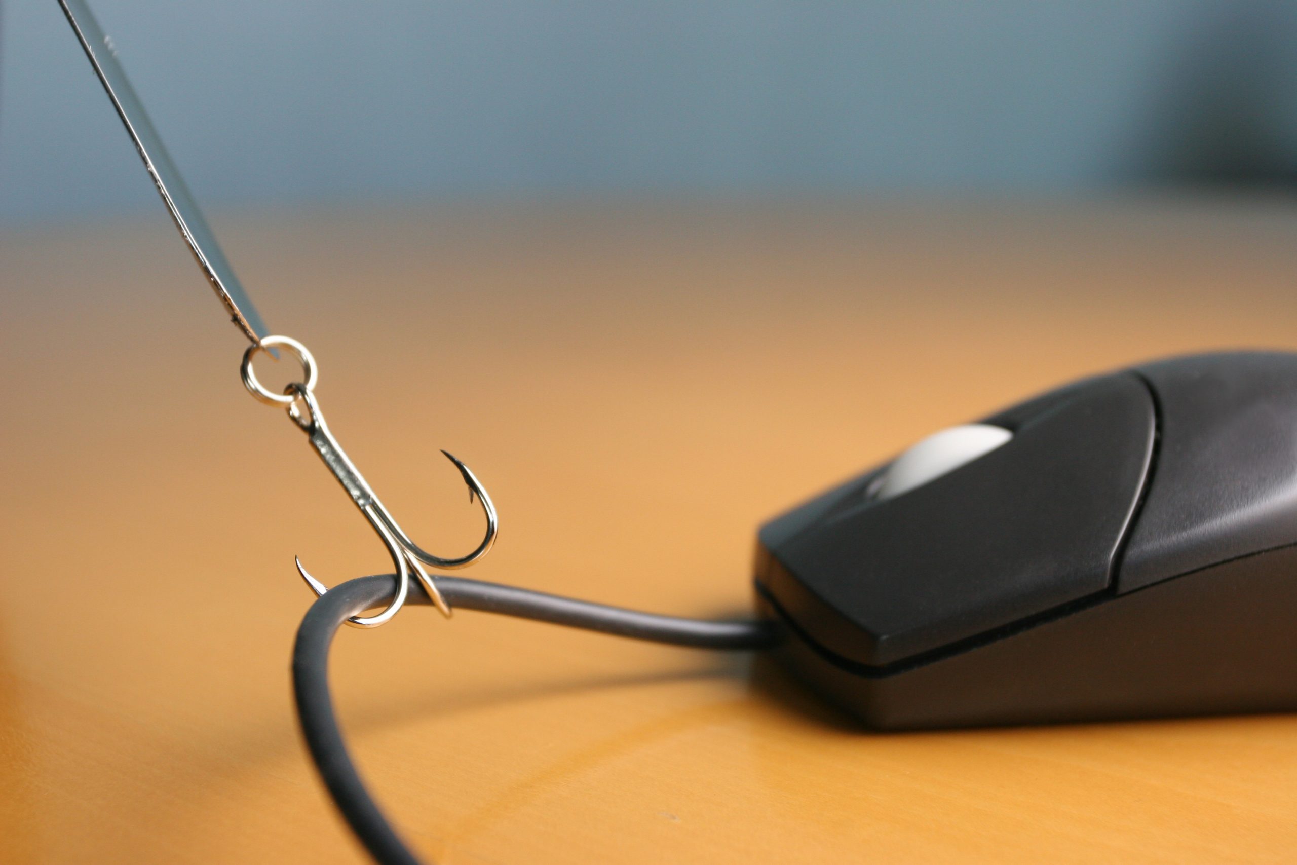 Close up of a fishing hook snagging a computer mouse cord on a desktop.