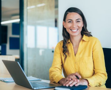 Confident businesswoman working on laptop at her workplace at modern office. Portrait of businesswoman in front of her laptop, looking at camera.
